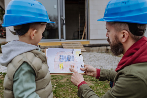 un uomo e un ragazzo con un casco blu che guardano un disegno su una cartella