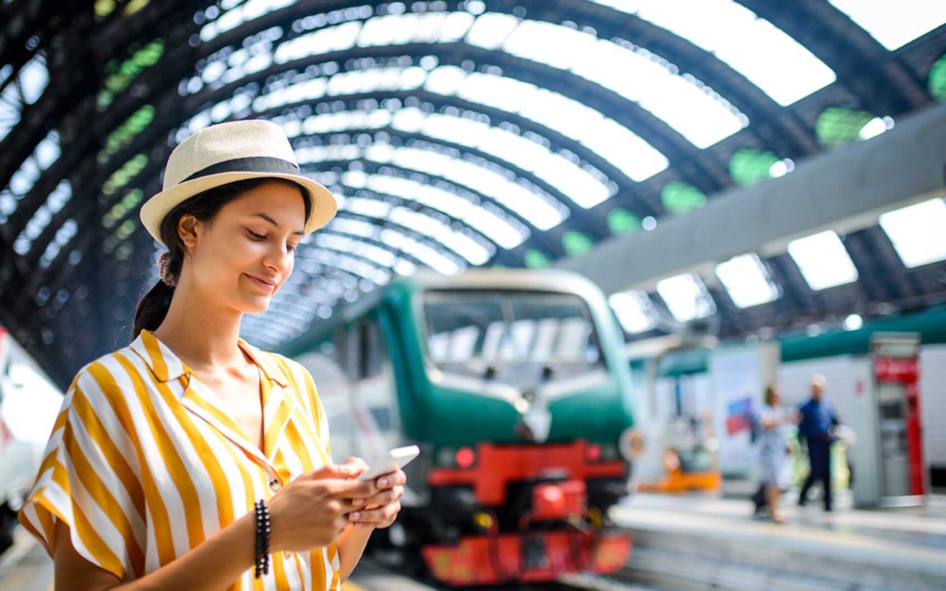 una donna con un cappello che guarda un telefono alla stazione dei treni
